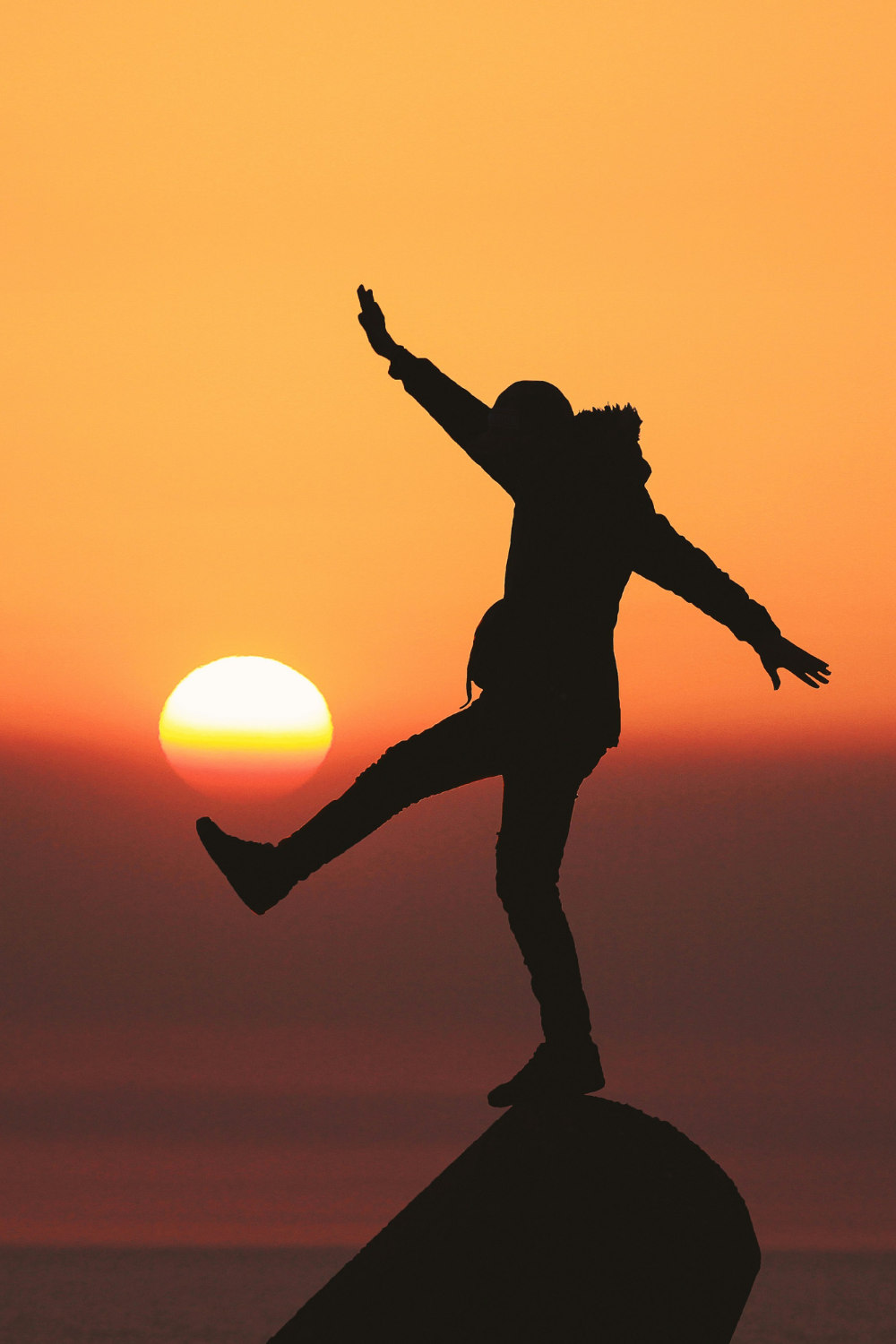 Person standing on a mountain top, playfully "kicking" the sun at sunrise