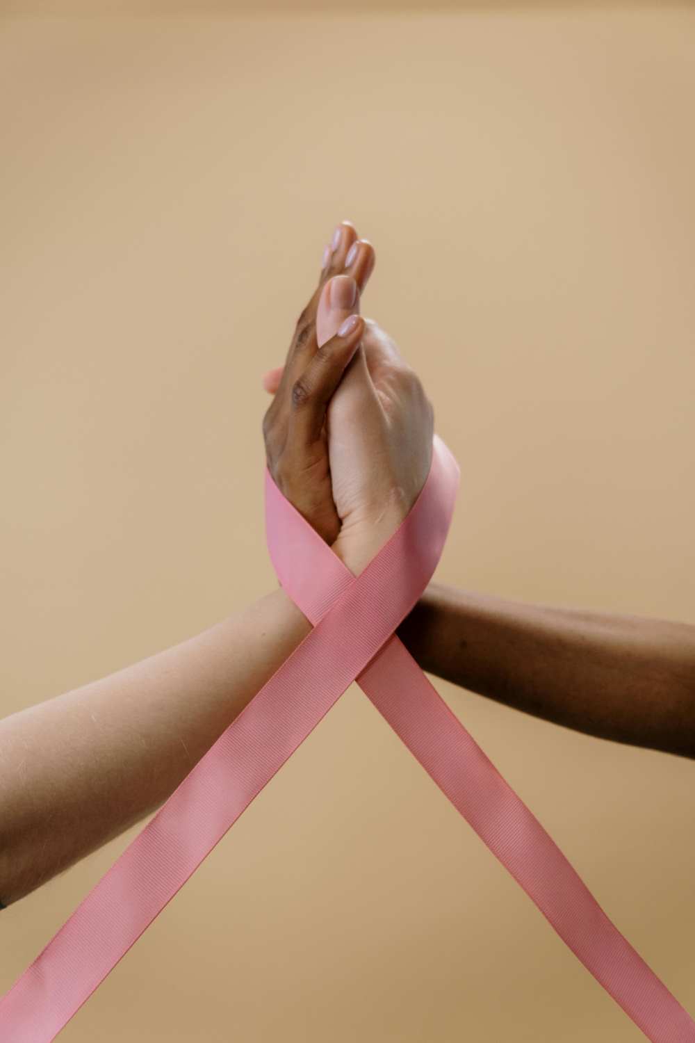 Male and female hands gently clasped, wrapped in a pink ribbon symbolizing breast cancer awareness, unity, and healing.