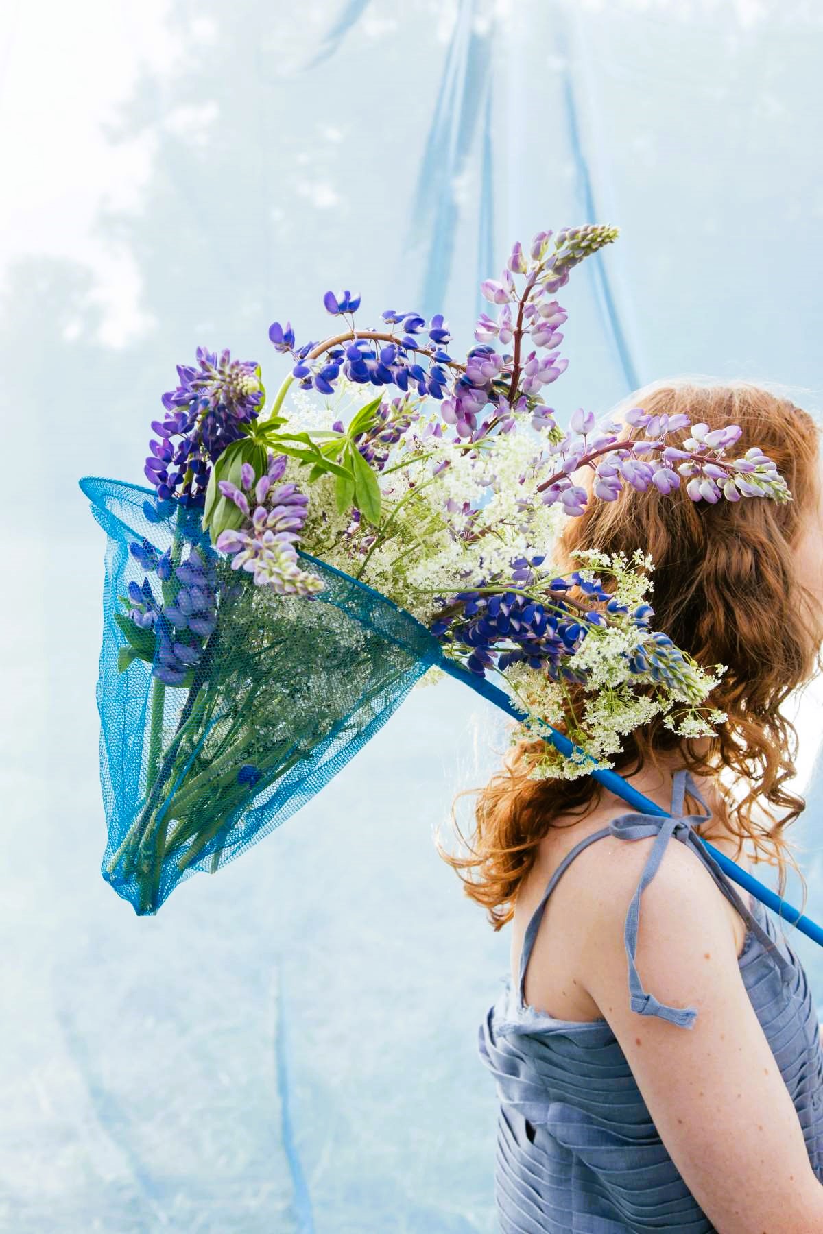 A calming blue-toned image featuring a woman carrying colorful flowers.