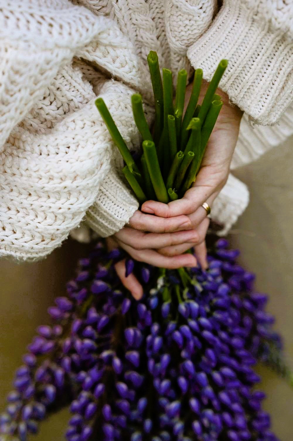 A woman holding a vibrant bouquet of purple flowers behind her back.