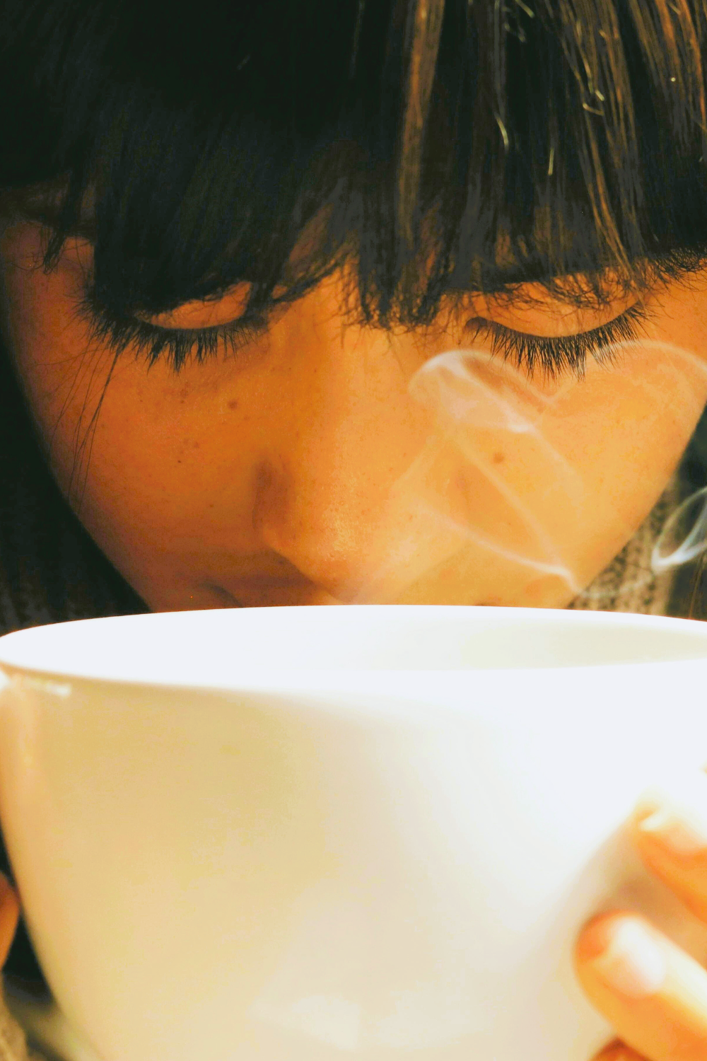 A woman holding a steaming tea cup.