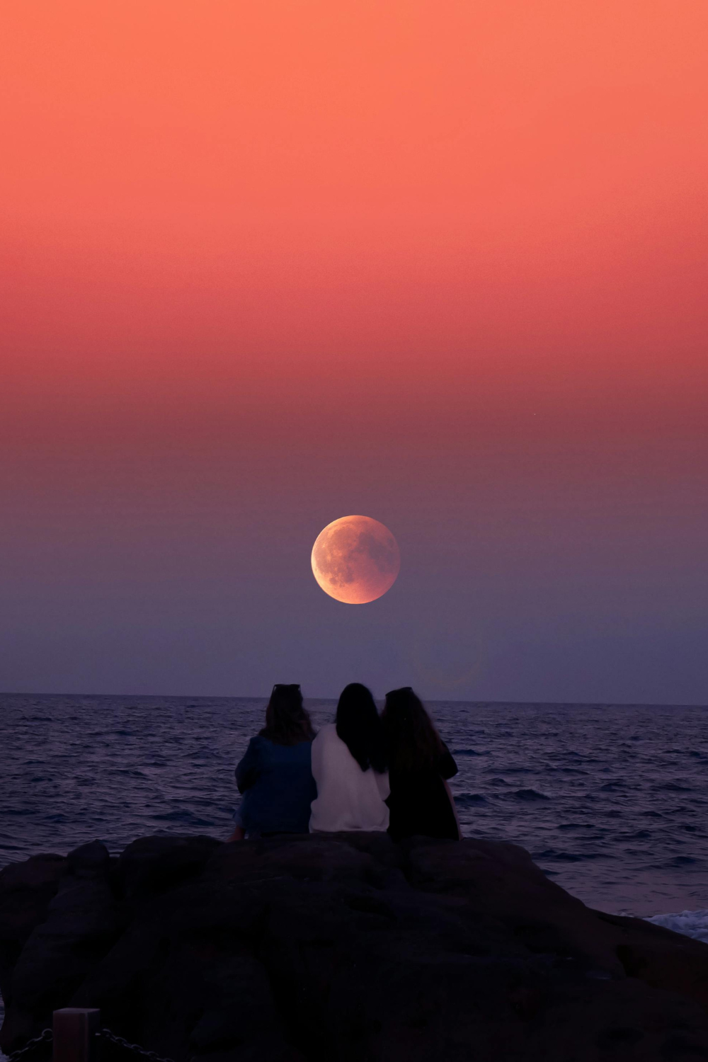 Three friends seating together under a glowing full moon in a vivid red sky