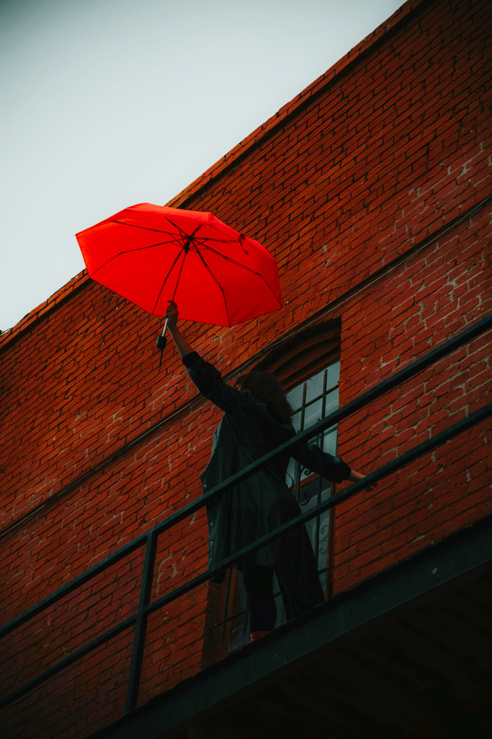 Silhouette of a person holding a red umbrella stands against a urban backdrop.