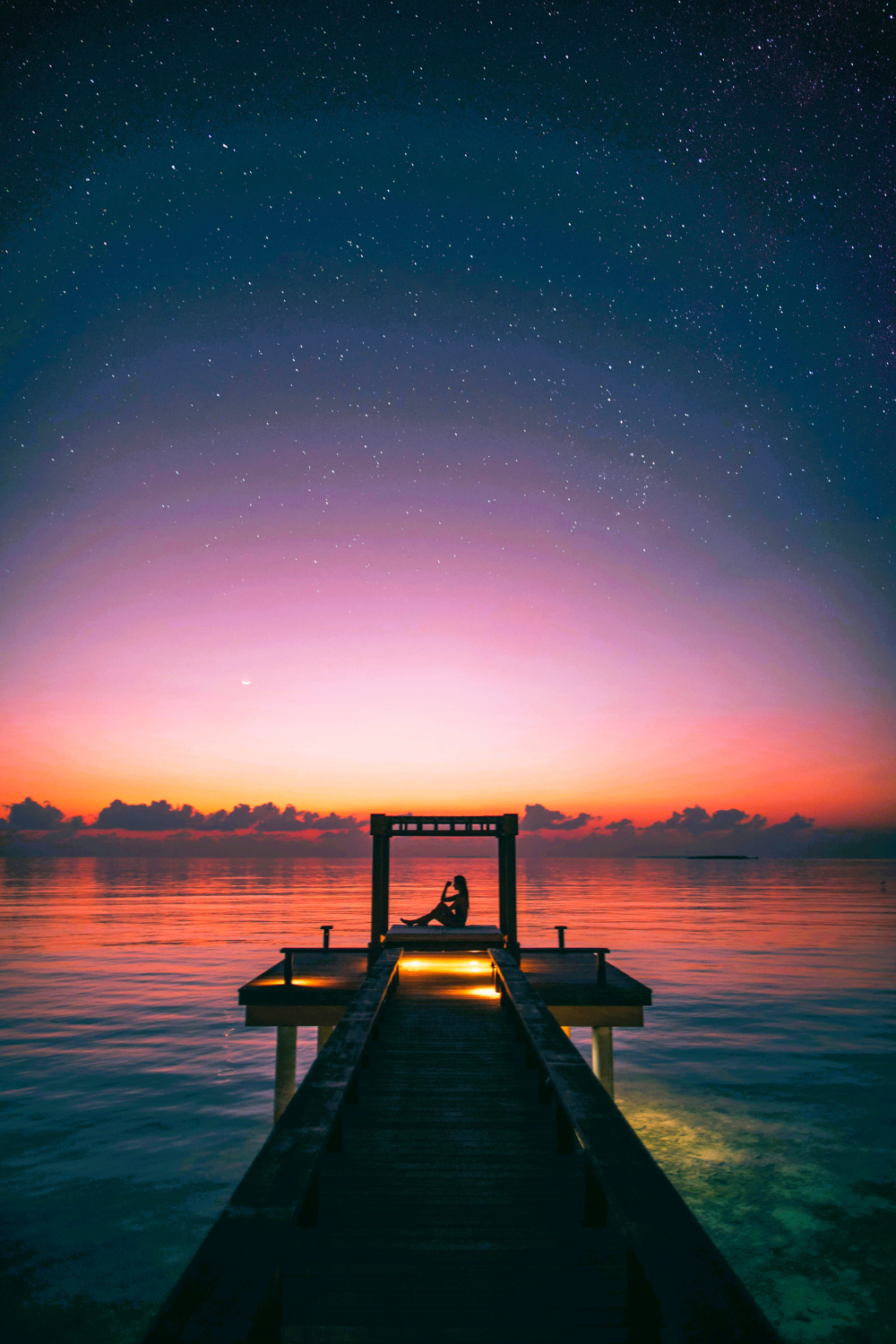 A serene night sky reflecting on the calm waters of the shore