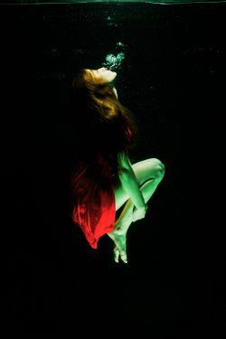 A woman in a flowing red dress gracefully dives into deep blue water,